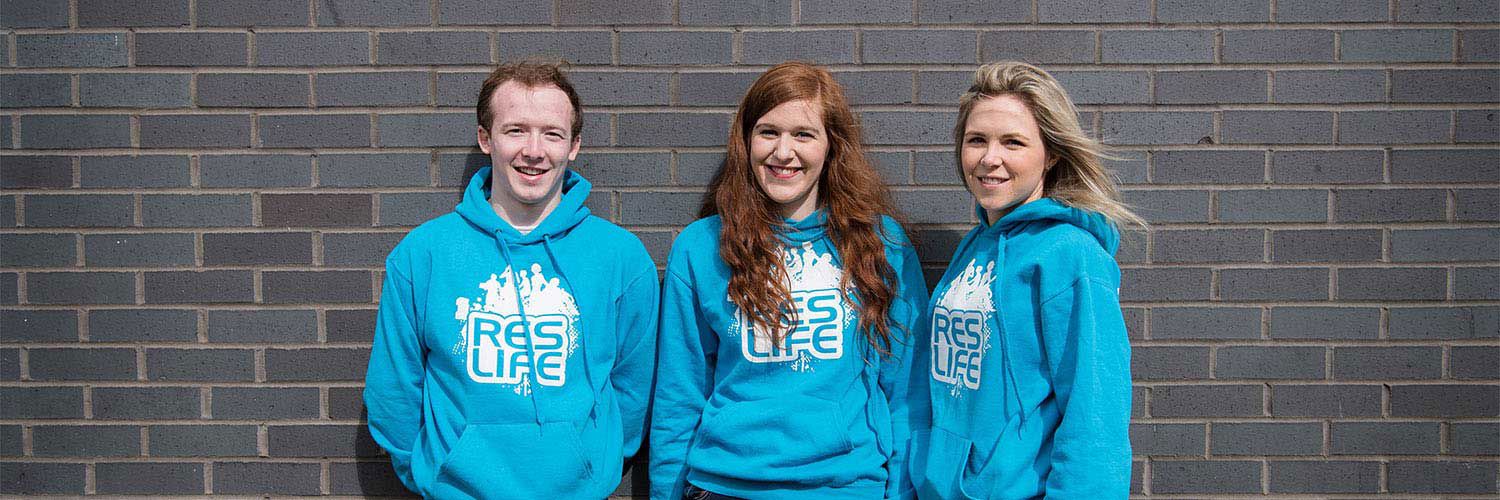 Three QMU students in matching blue sweaters smiling for the camera