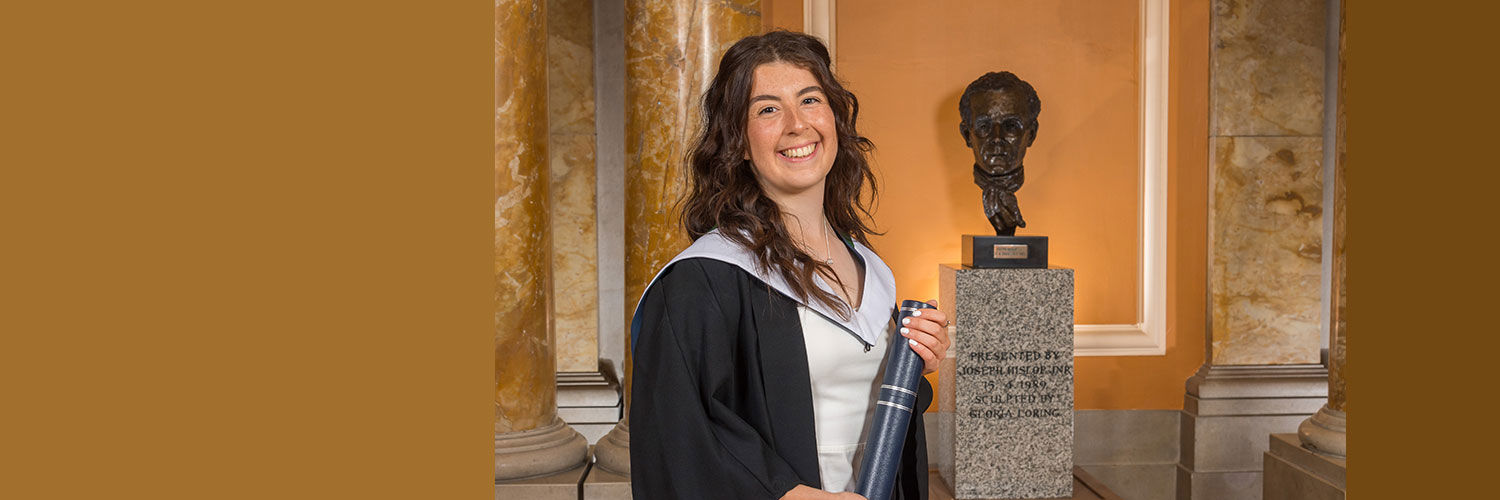 Portrait photo of Rachel Dorrat wearing her graduation robe and holding her graduation scroll
