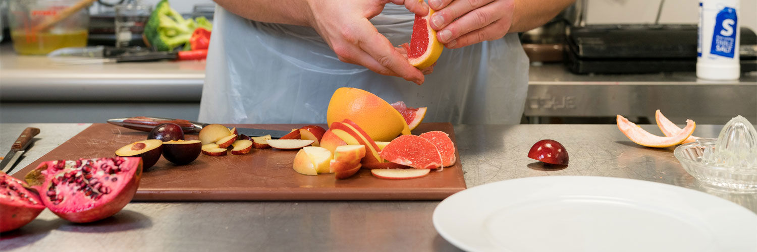A person chopping various different fruits on a chopping board.