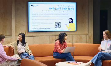 Four students sit on the curved, S-shaped sofa in the reception area of the library.