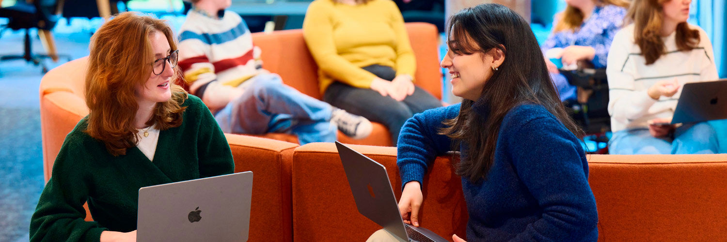 Two students smiling and chatting while working on a laptop