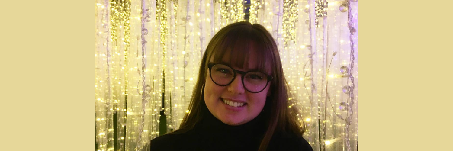 Queen Margaret University student Bailea Jackson stands in front of a background made of fairly lights.