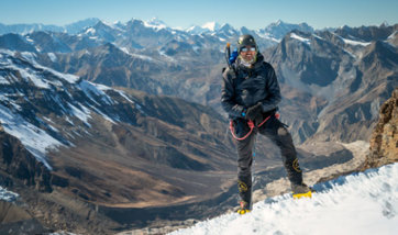 Mostafa Salameh stands on the top of a snowy mountain range in hiking gear.