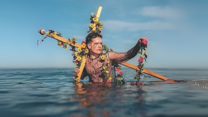 Man in the sea holding a wooden cross on his back