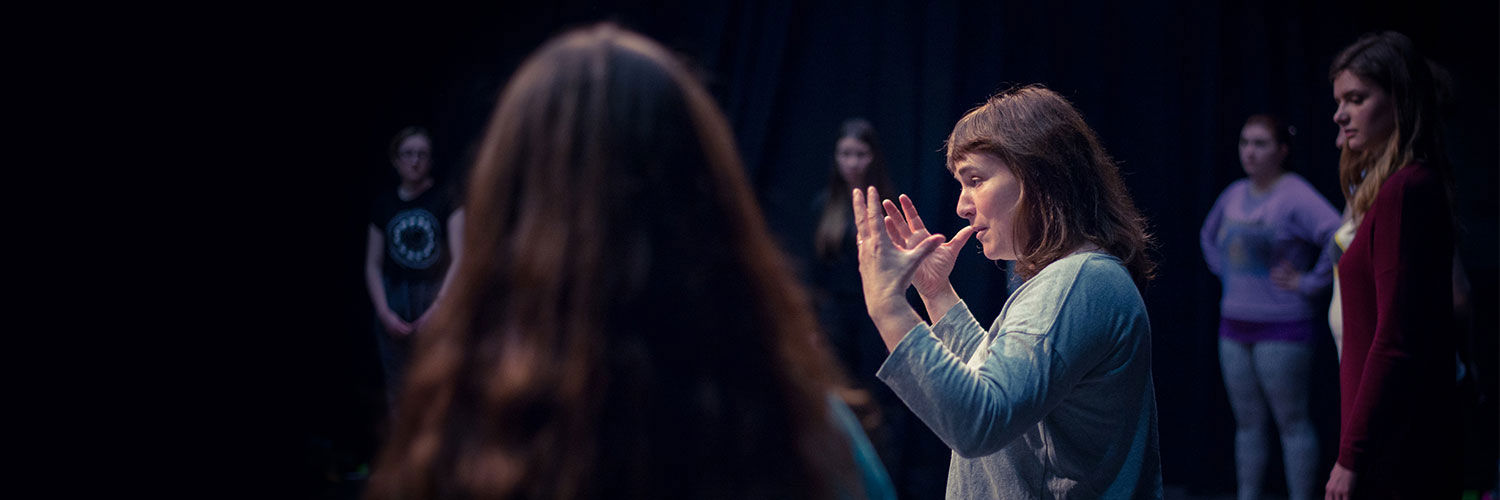 A lecturer in drama stands on stage giving instructions to students