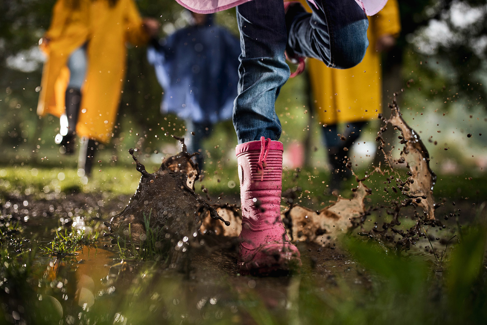 Close up photo of a child's boot jumping into a muddy puddle