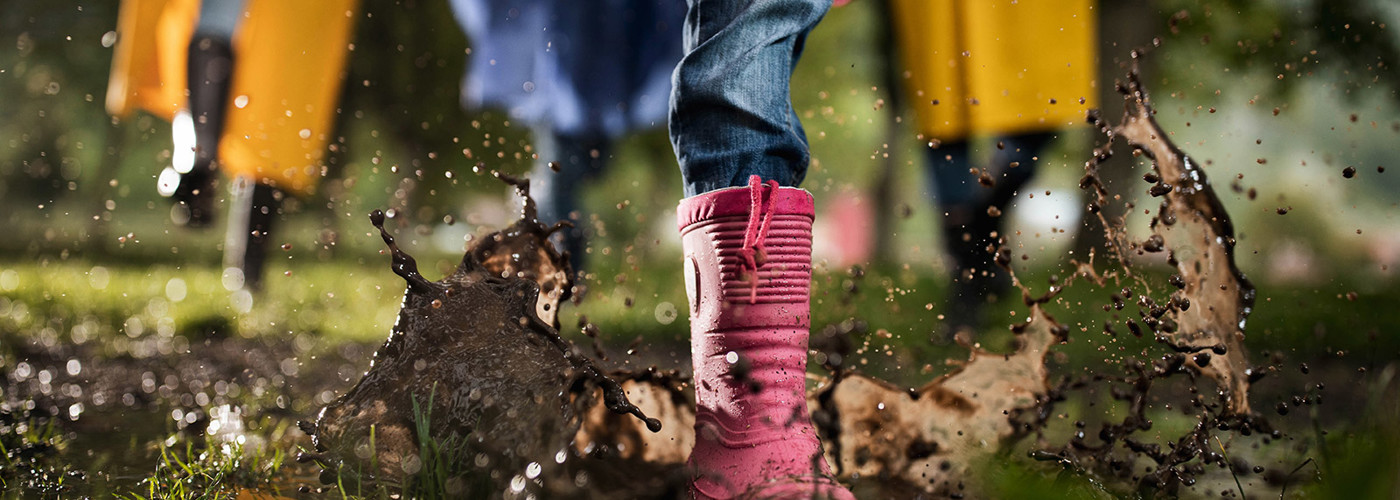 Close up photo of a child's boot jumping into a muddy puddle