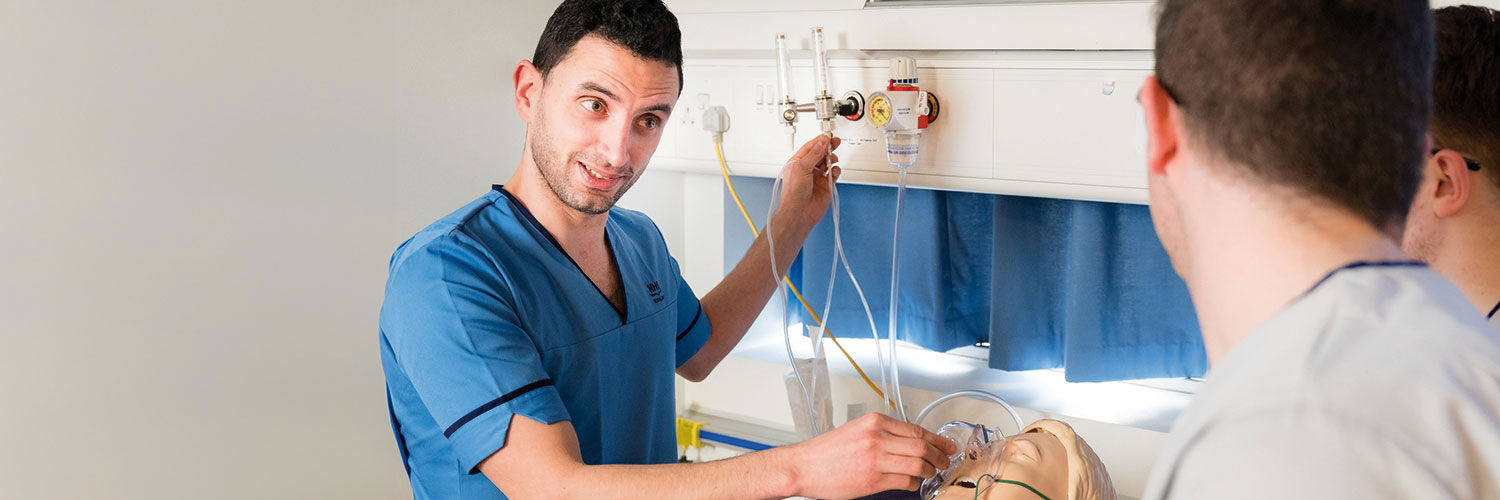 Three male nurses working in one of the nursing demonstration suites on campus.