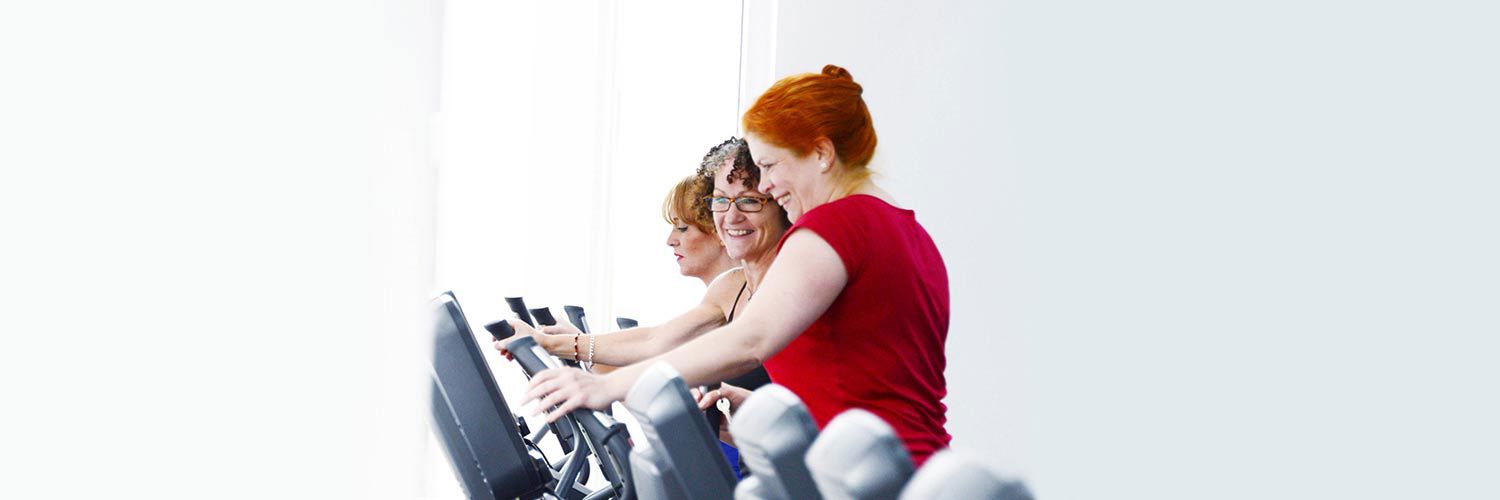 Two women smiling and looking at the screen of the exercise machine one of them is using