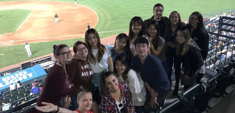 A group of people pose for a photo in the stands of a baseball pitch.