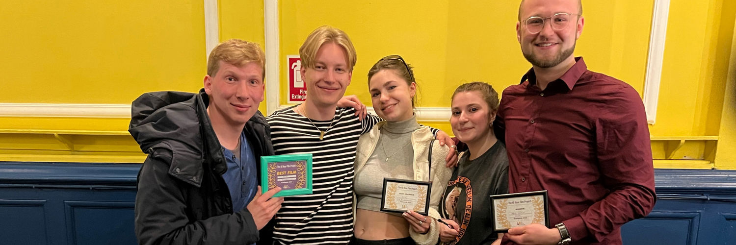 A group of students in their 20s are smiling at the camera and holding framed awards at a local film event in Edinburgh.
