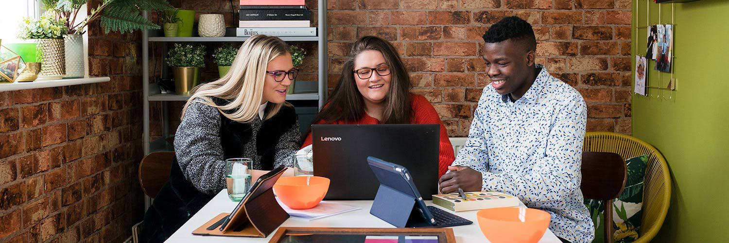 Two female and one male student working together on their laptops at home.