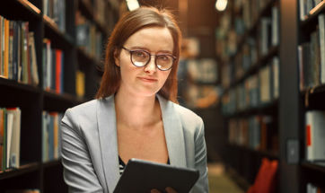 A female student sat on the library floor, surrounded by bookcases