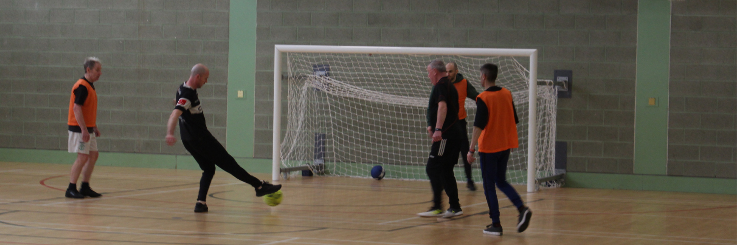 Five men playing walking football in an indoor football pitch