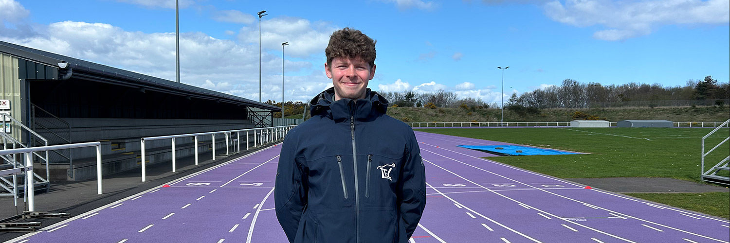 Head and shoulders image of young man with backdrop of athletics track