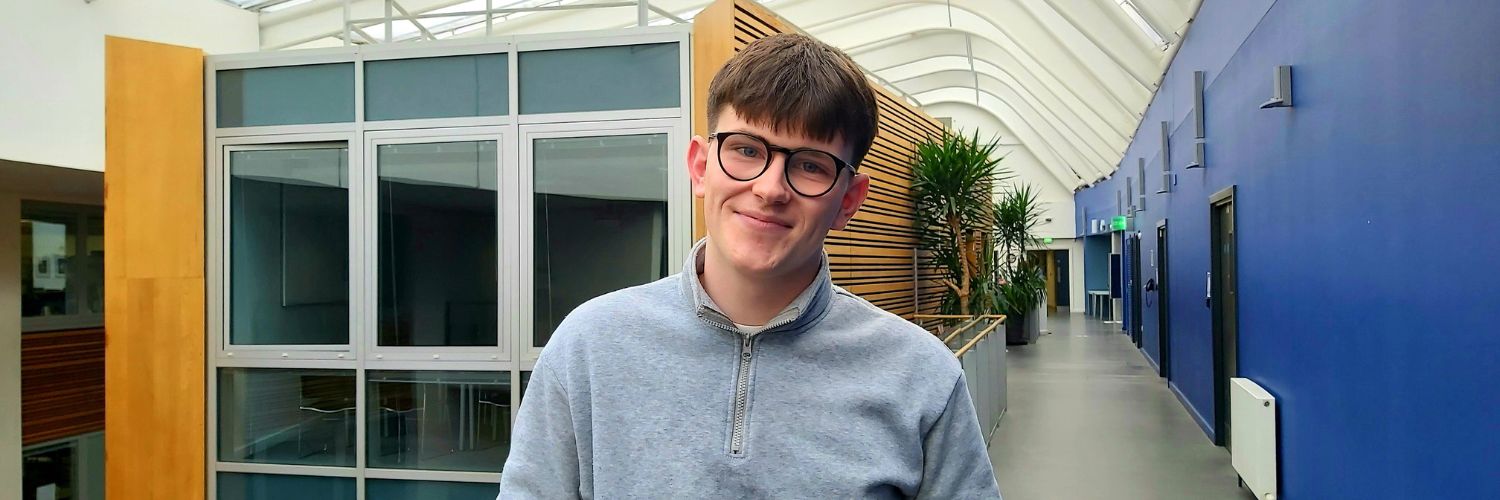 Head and shoulder shot of male student with the backdrop of the interior of Queen Margaret University
