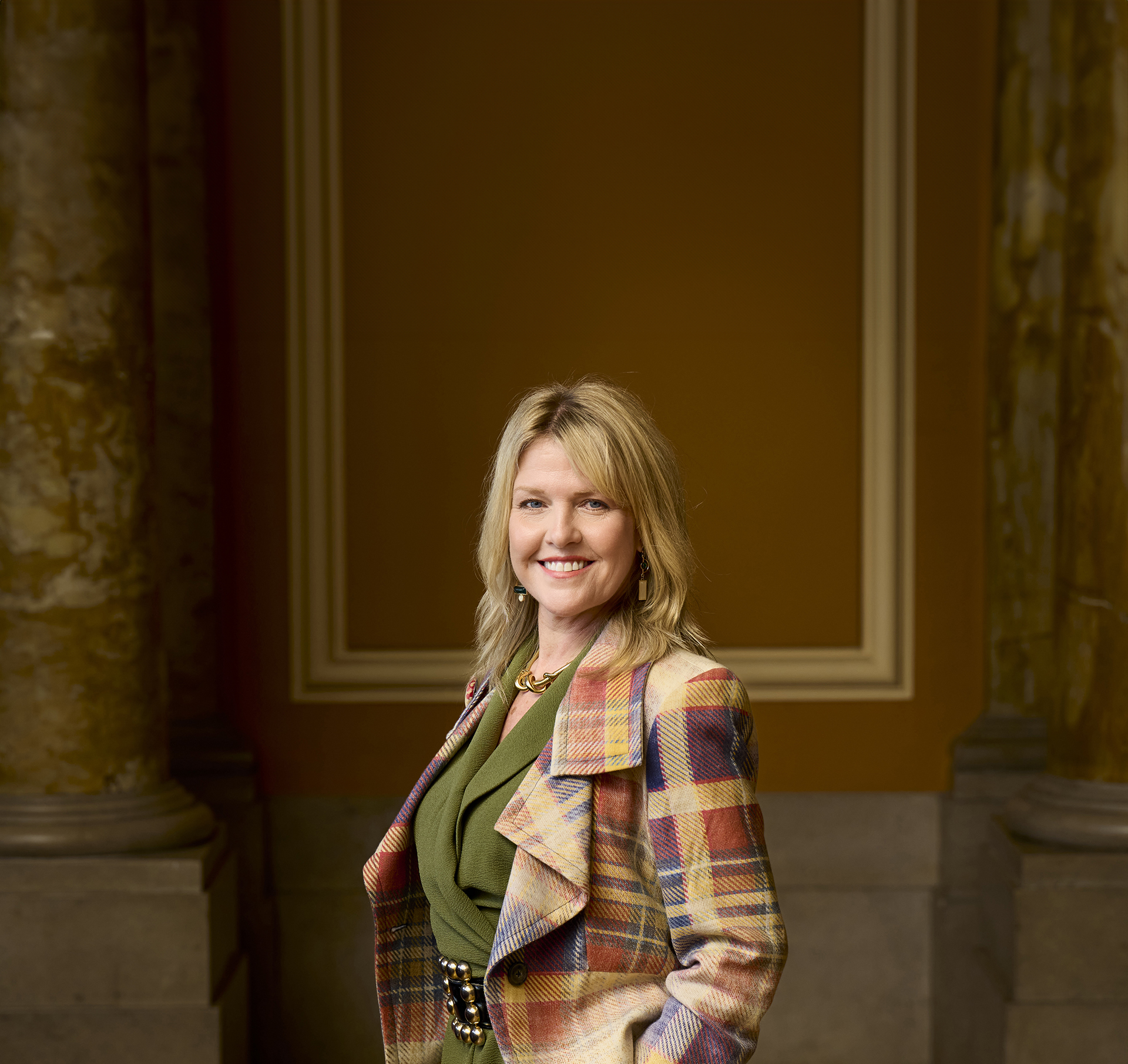 Photo of Ashley Jensen smiling at the camera wearing a stylish tartan jacket