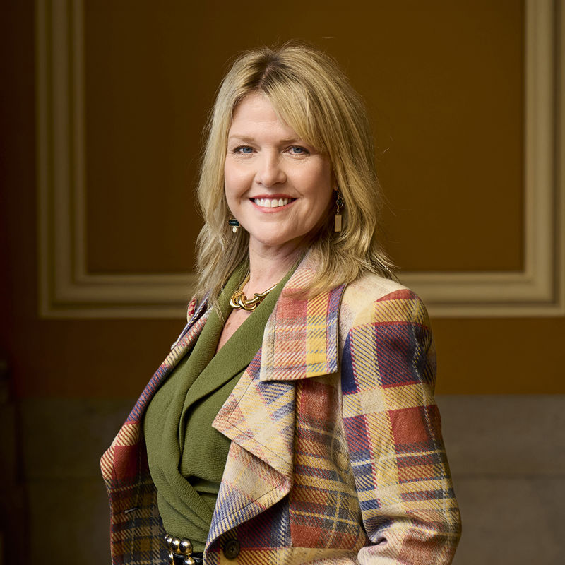 Photo of Ashley Jensen smiling at the camera wearing a stylish tartan jacket