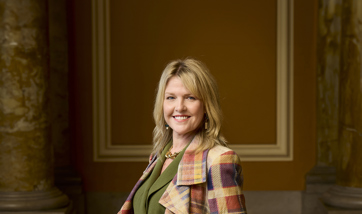Photo of Ashley Jensen smiling at the camera wearing a stylish tartan jacket