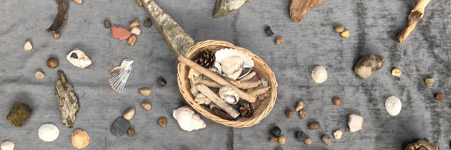 A grey blanket covered in stones and seashells with a basket in the centre