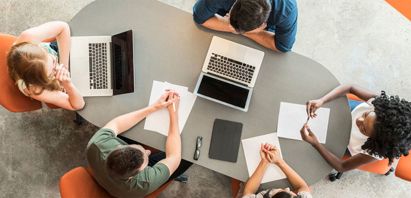 A group of people sat at a table, working on a project together. The photo is taken from above the table.