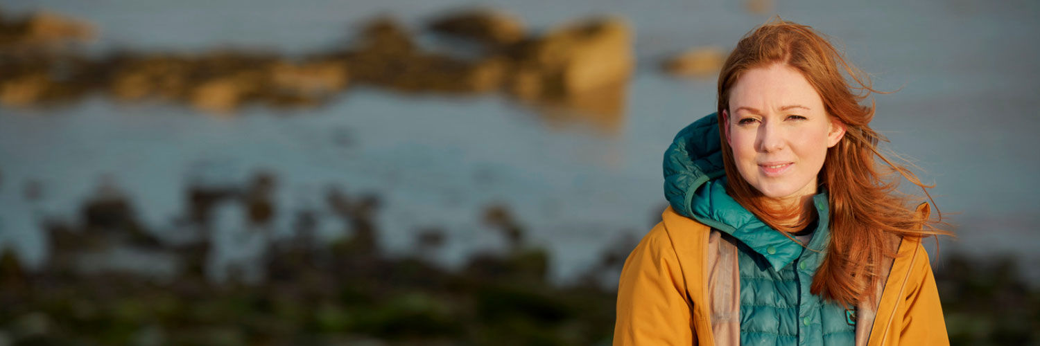 A woman with red hair sitting down on the beach