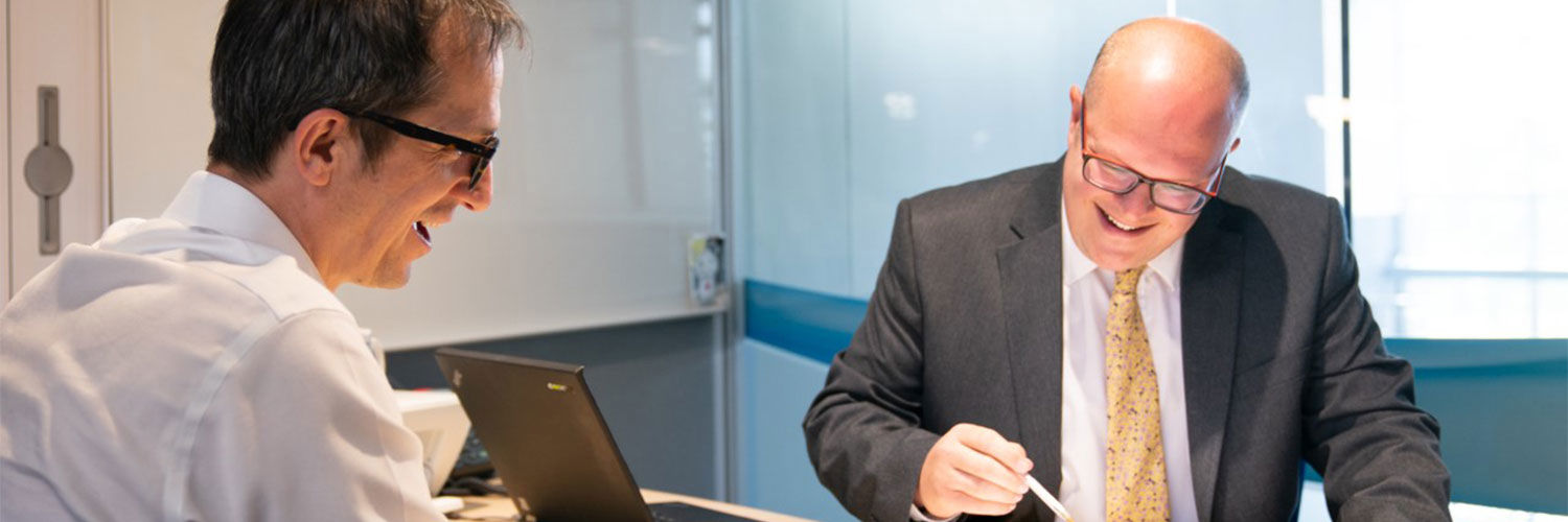 Image of two men smiling over paperwork