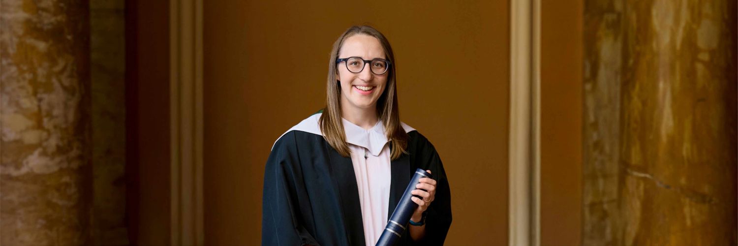 Portrait shot of smiling girl wearing graduation robes and holding graduation scroll