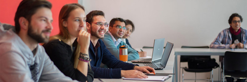 A group of students sitting in the classroom, looking towards a lecturer who is off screen.