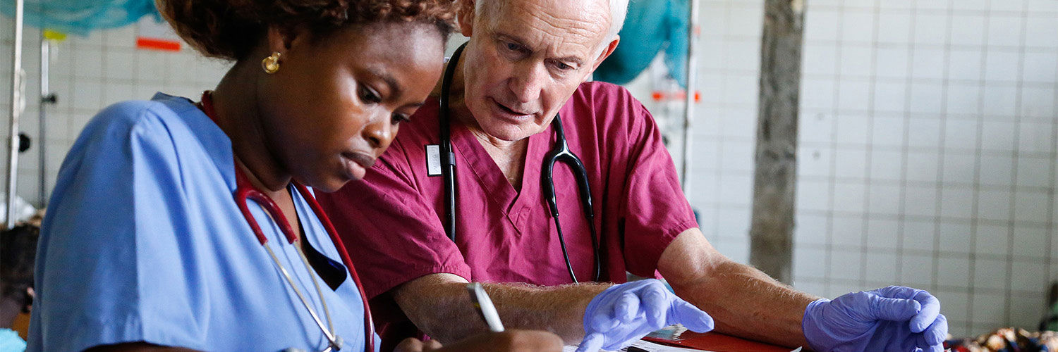 Two nurses sitting together in scrubs checking some paperwork