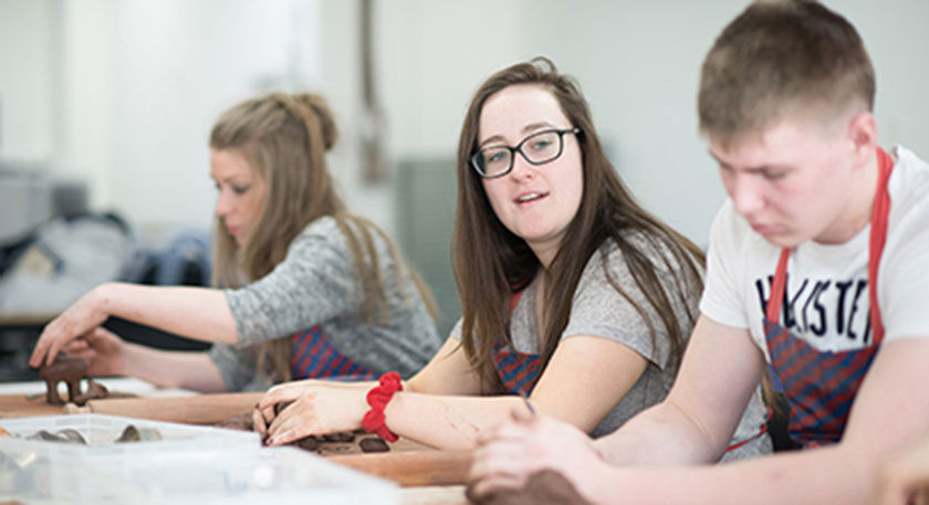 Close up of a row of students with aprons on moulding clay