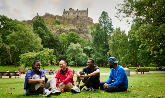 International students sitting on grass in front of Edinburgh Castle