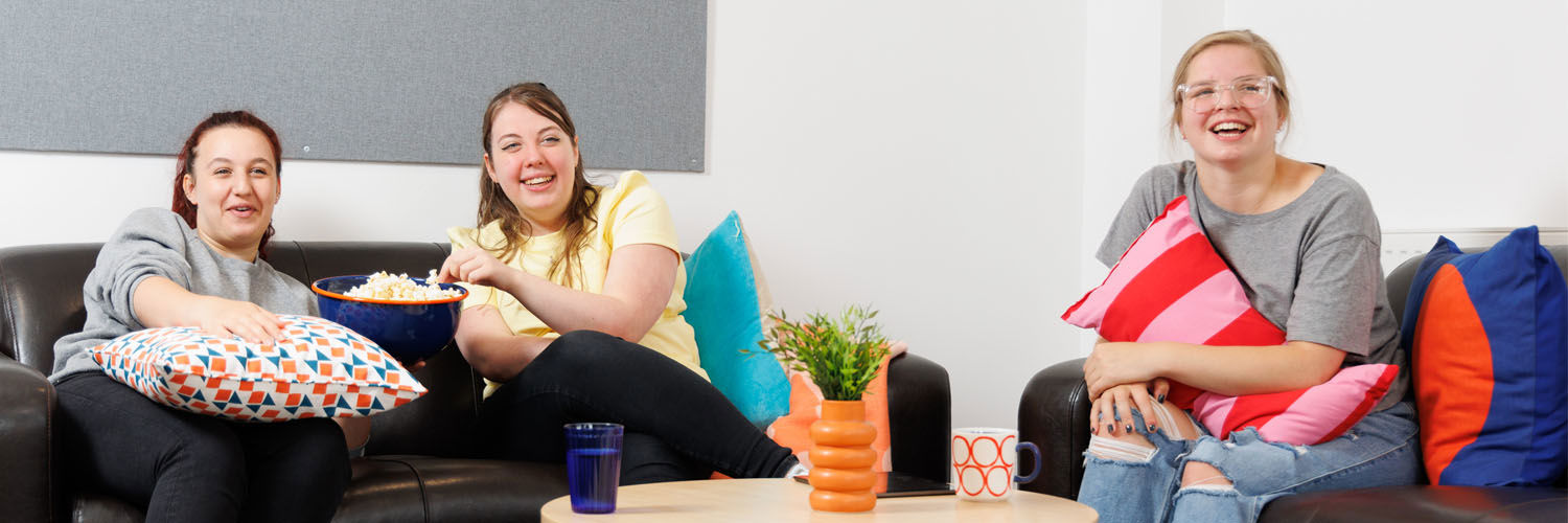 Three female students enjoy popcorn while watching a film in their QMU Student Accommodation