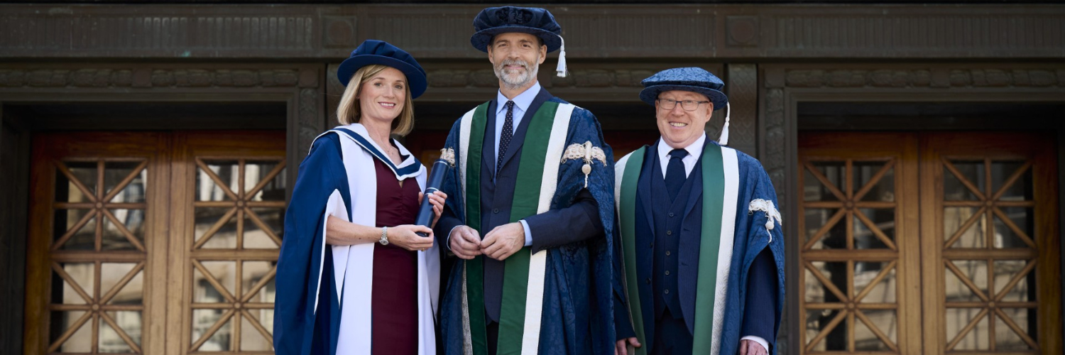 Three individuals in graduation gowns smiling looking towards the camera