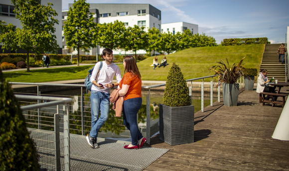 QMU students chatting beside a pond on a university campus in the sunshine