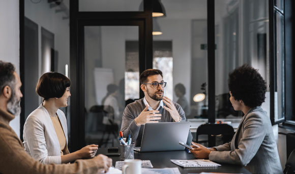 A group of working professionals sit at a meeting table having a lively discussion.