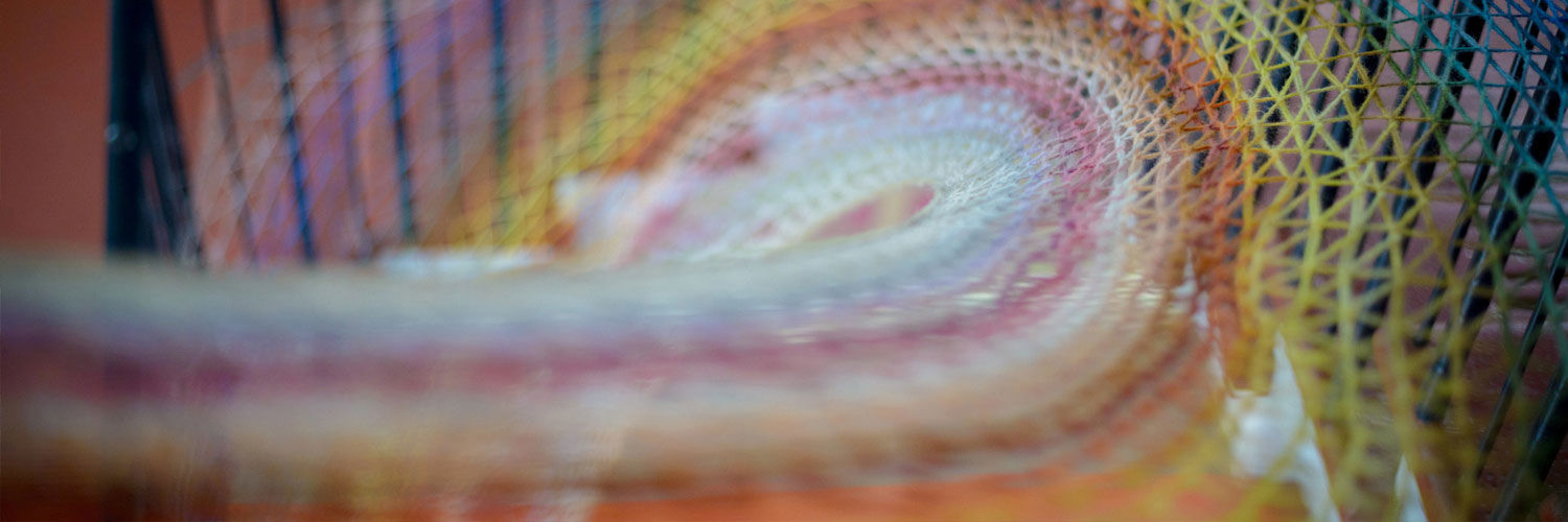 A close-up shot of a rainbow coloured piece of yarn work. The yarn appears to form a curved pattern suspended in the air.