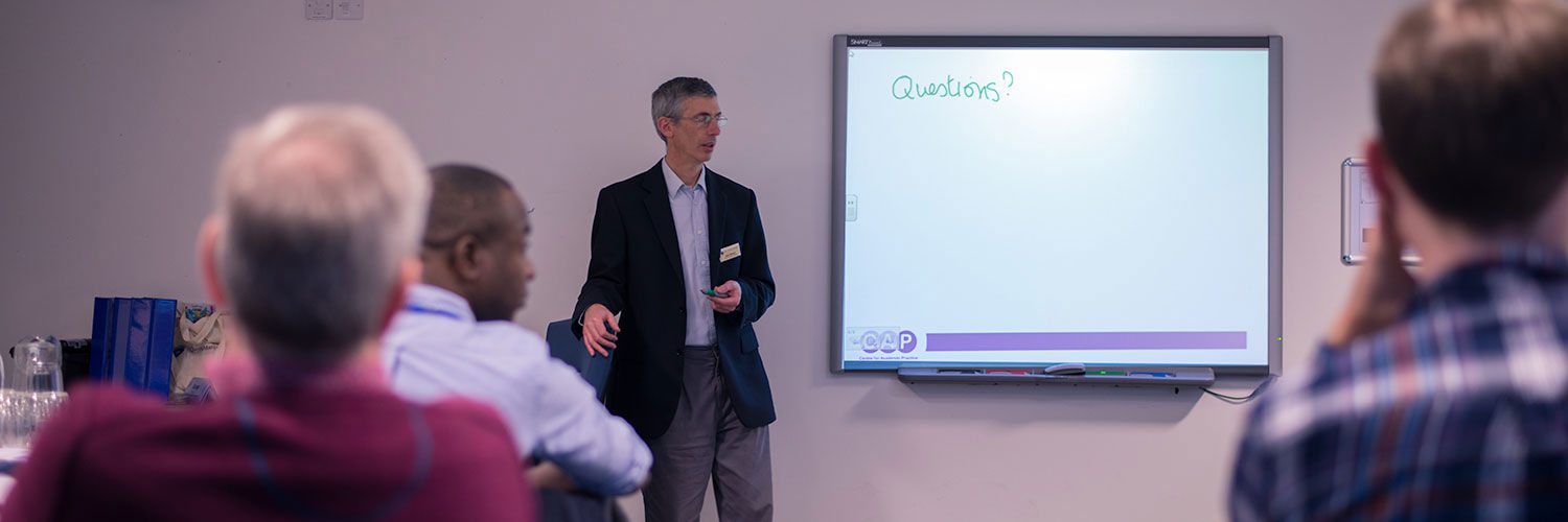 Photo taken from the back of the room during a presentation, the board says "questions?"