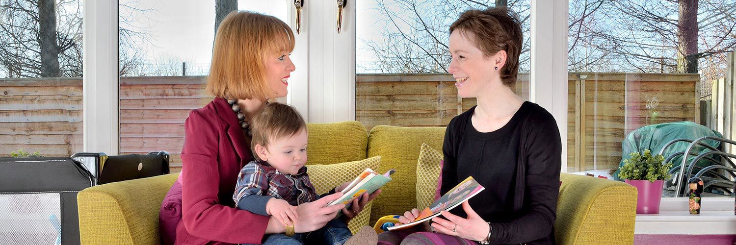 A mother and young son speaking on their sofa at home to a health visitor