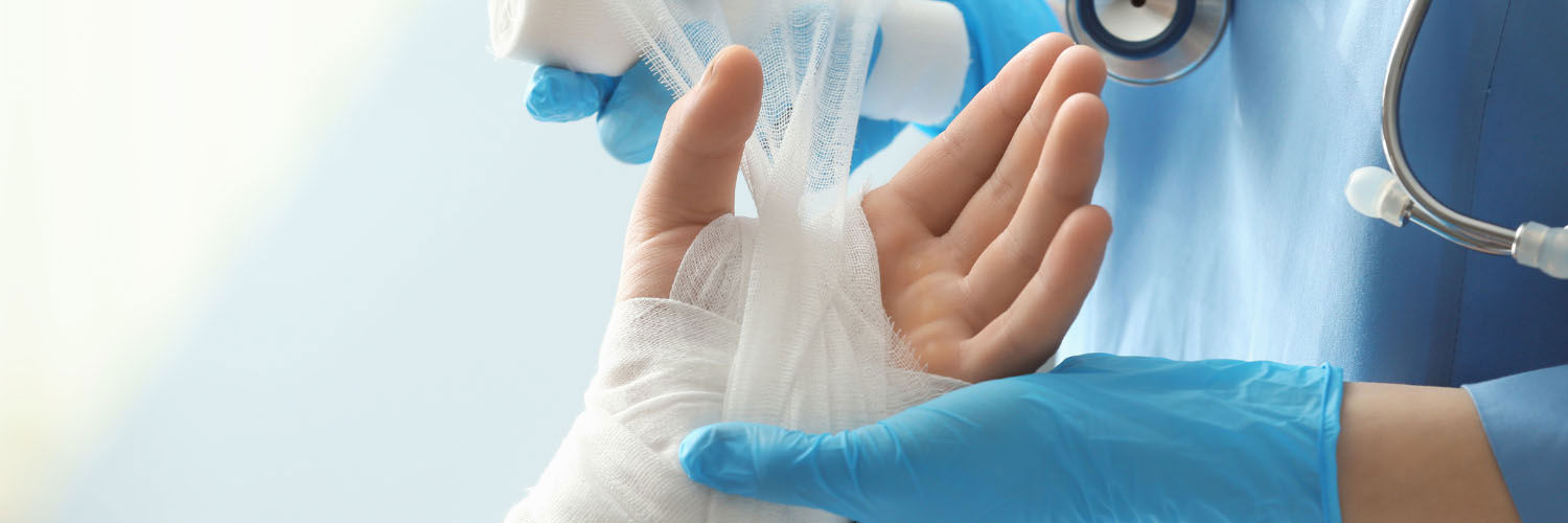 A nurse wraps a gauze dressing around a patient's hand and wrist.