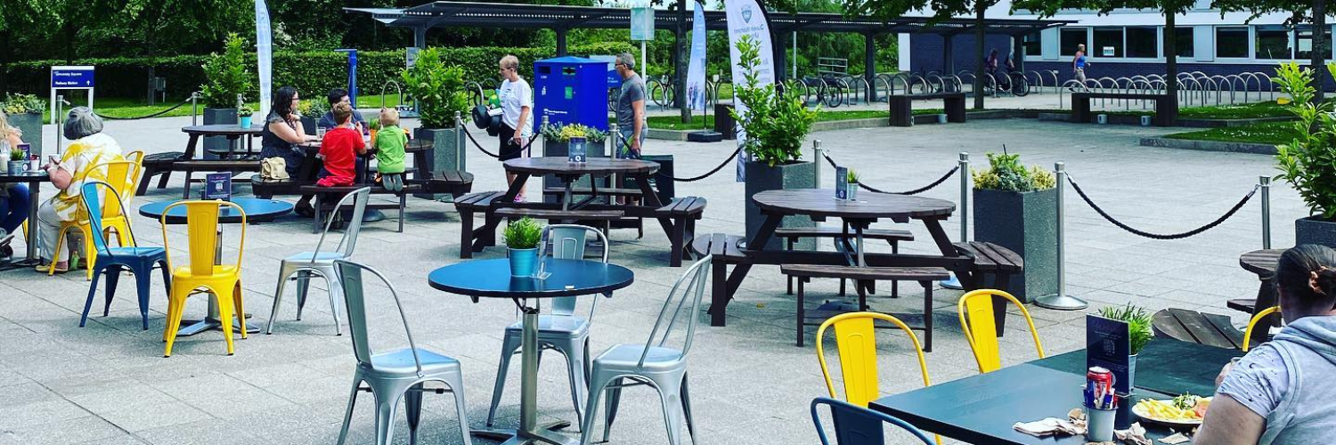 A family with young children sitting at picnic tables in QMU's University Square