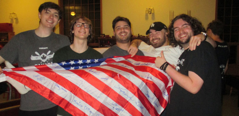 Four students holding another one up lengthways that is draped in a flag of the USA.