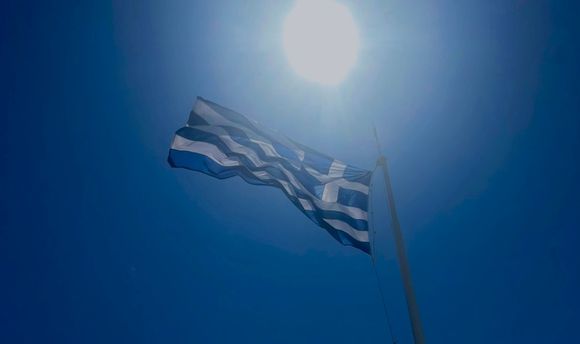 A Greek flag flown against a bright blue sky