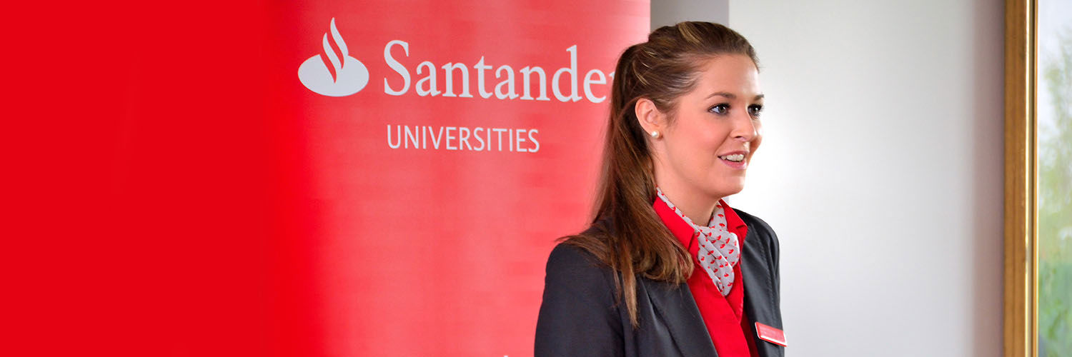 A Santander employee smiling in front of a Santander Universities sign