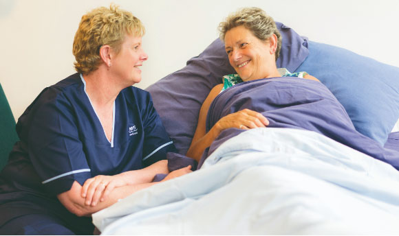 A female nurse tends to a woman lying in bed.