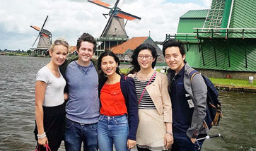 A row of smiling students posing for a photo by some windmills in Holland