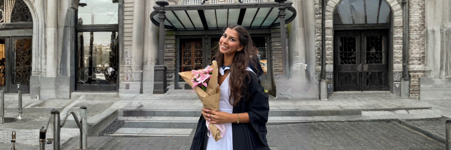 Female student holding flowers wearing graduation robes standing outside the Usher Hall.