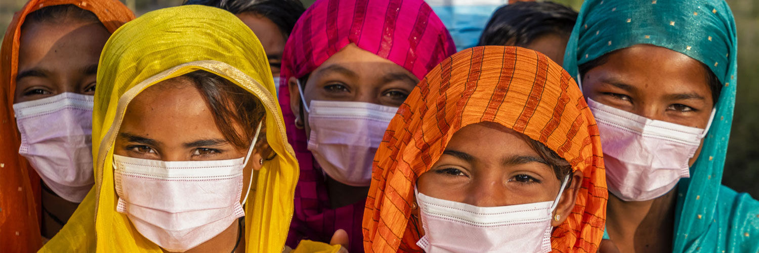 A large group of mostly young women wearing brightly coloured headscarves and white surgical masks.
