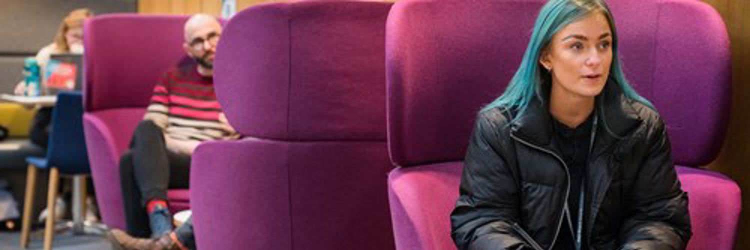 Student with vibrant blue hair sat on purple pod seat in QMU Atrium