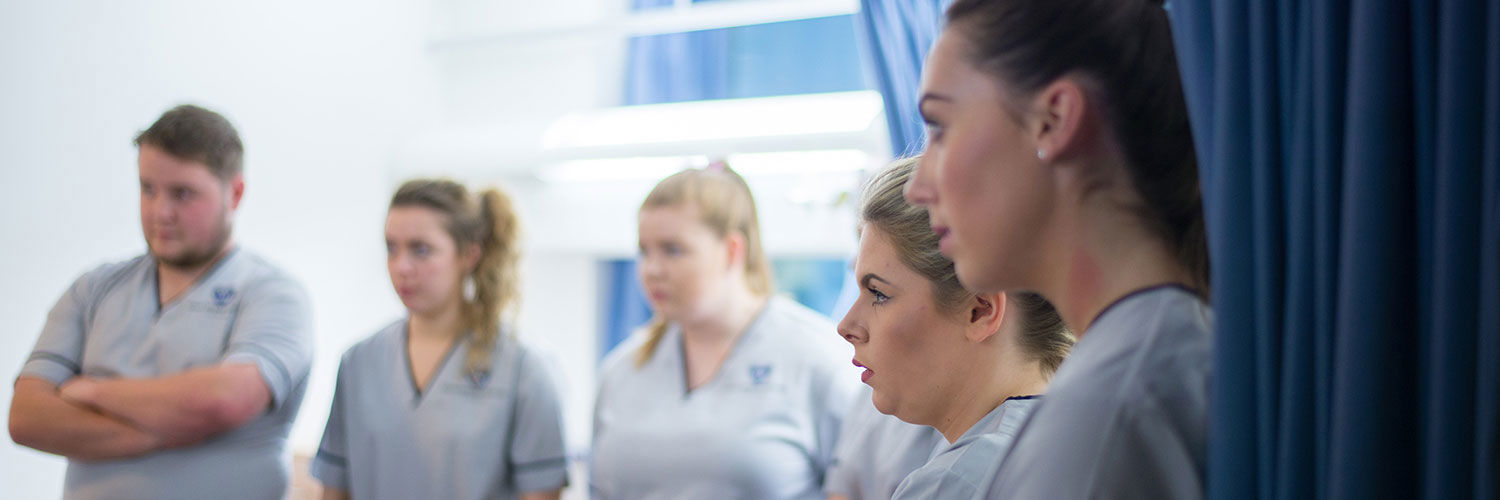A row of QMU student nurses listening intently as a senior nurse speaks to them